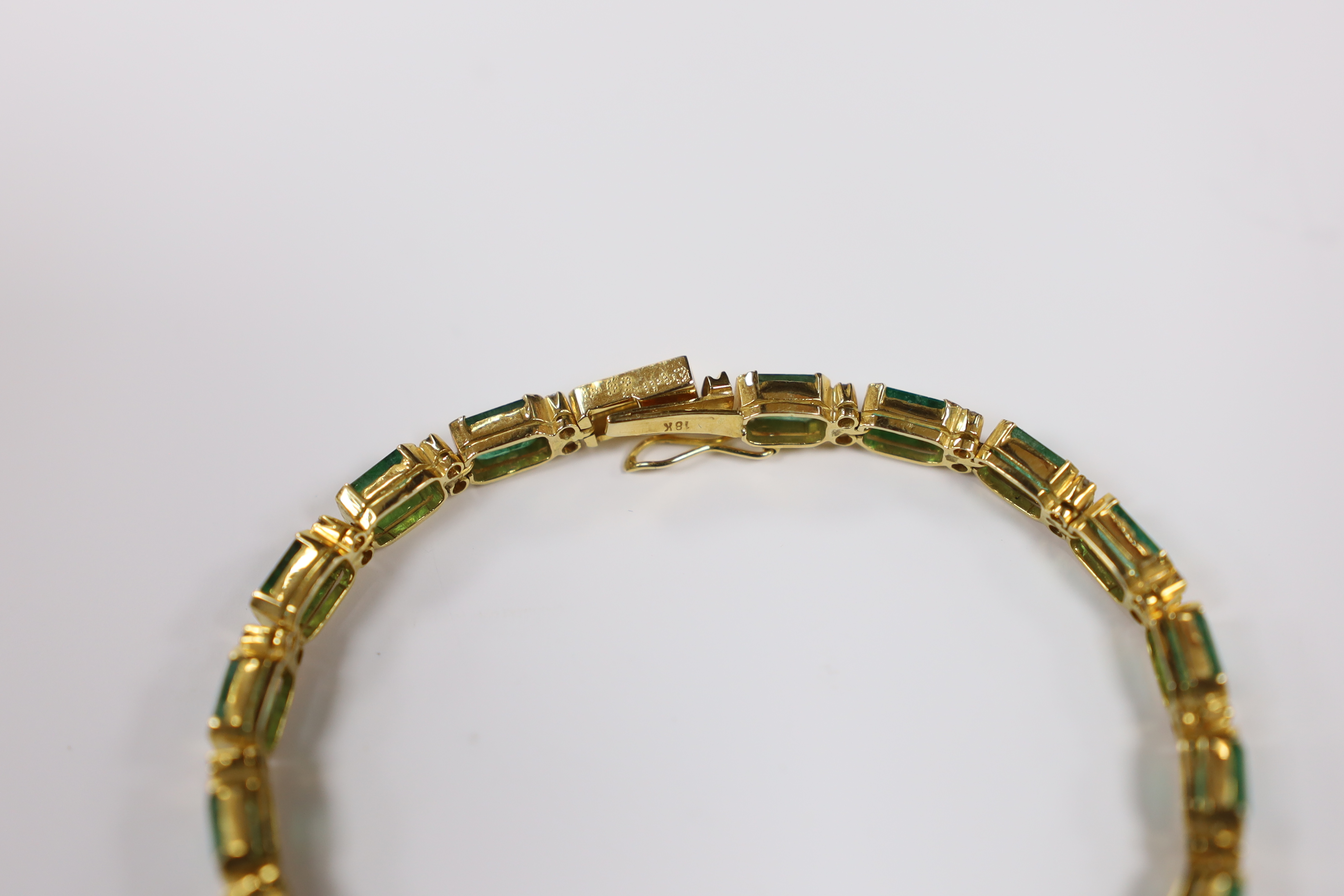 A modern 18k yellow metal and twenty stone emerald set line bracelet, with diamond chip spacers, 18cm, gross weight 13.5 grams.